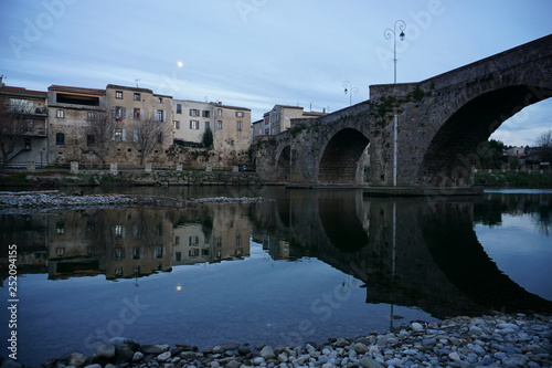mirror reflection of an old stone bridge and waterfront by the river at dusk with the full moon in France 