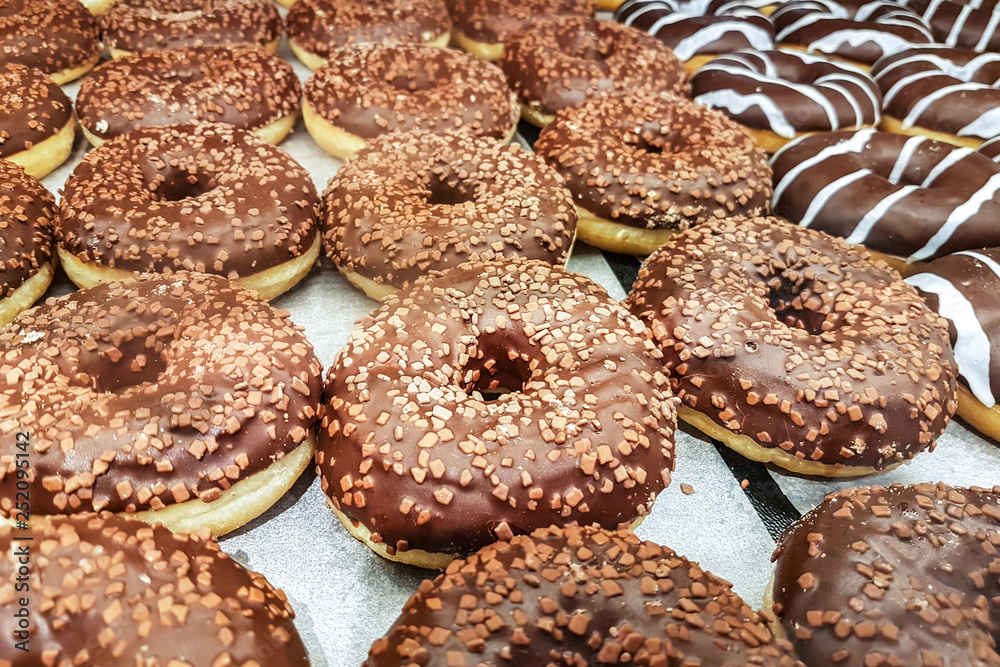 Group of sweet donuts in a rows with chocolate and sprinkles for sale in a grocery.