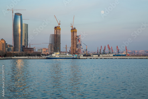 Baky skyline view from Baku boulevard the Caspian Sea embankment . Tall buildings in Baku. Ship cranes . Moon. harbor . Port © Adil