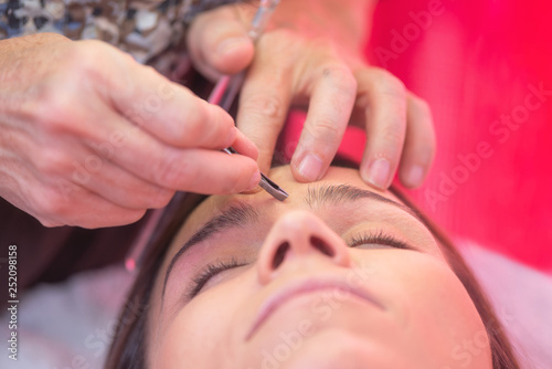 Young woman havind professional eyebrow correction at spa salon .