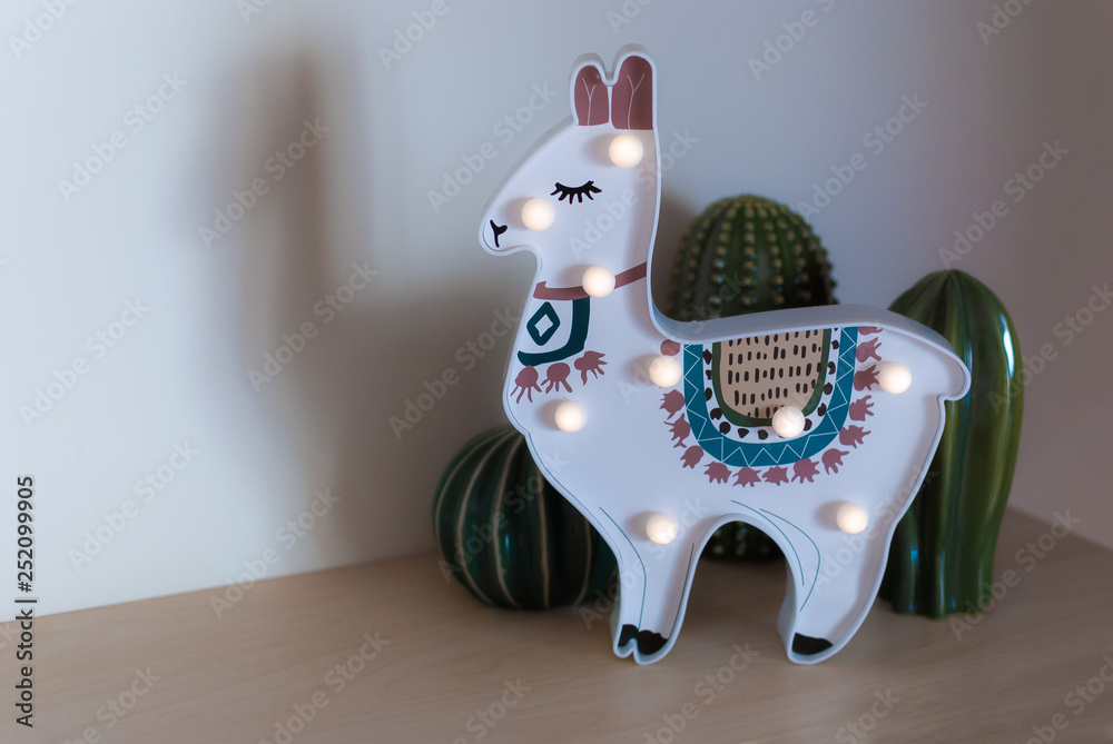 A trendy llama kids night lamp standing on a bedside in dawn or sunrise  light with ceramic cactuses behind it Stock Photo | Adobe Stock