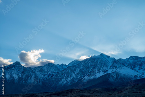 blue sky, clouds, slanted beams of sunlight over peaks of Eastern Sierra Nevada, California, USA © mariekazalia