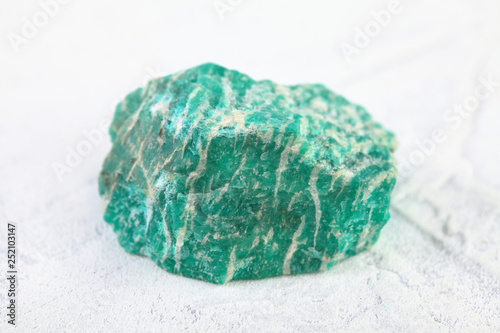 Natural rock amazonite mineral stone from Kola Peninsula on white cement background.