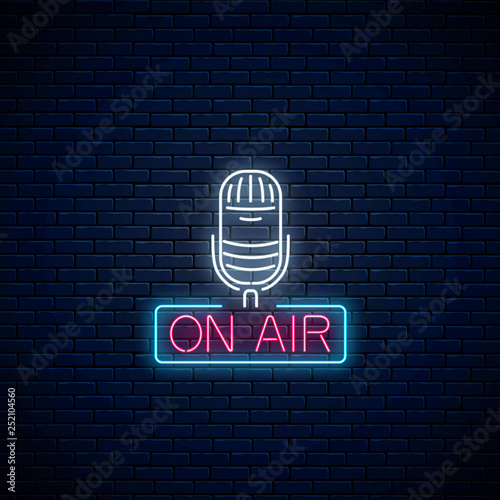 Neon on the air sign with microphone on dark brick wall background. Glowing signboard of radio station.
