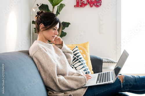 Woman sitting on her couch, surfing the net, using laptop photo