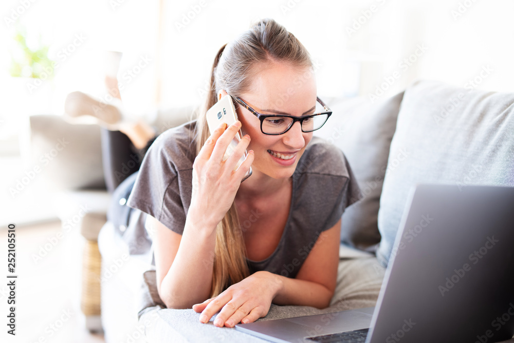 Junge Frau telefoniert mit dem Smartphone und schaut in ihren Laptop 