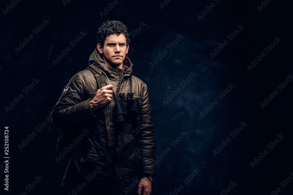 Young manly brutal hipster posing and looks into camera on black background in studio Young manly brutal hipster posing and looks into camera on black background in studio