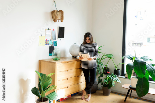 Young woman standing at commode at home reading a booklet