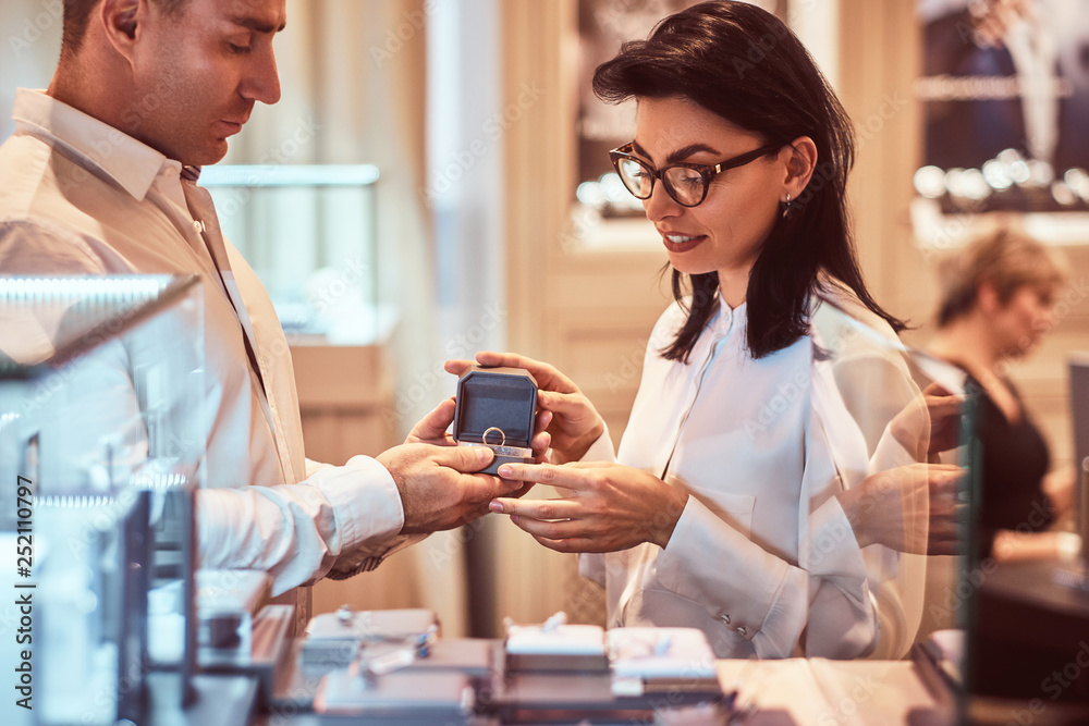 Elegantly dressed male and his girlfriend choose wedding rings in a luxury jewelry store Elegantly dressed male and his girlfriend choose wedding rings in a luxury jewelry store