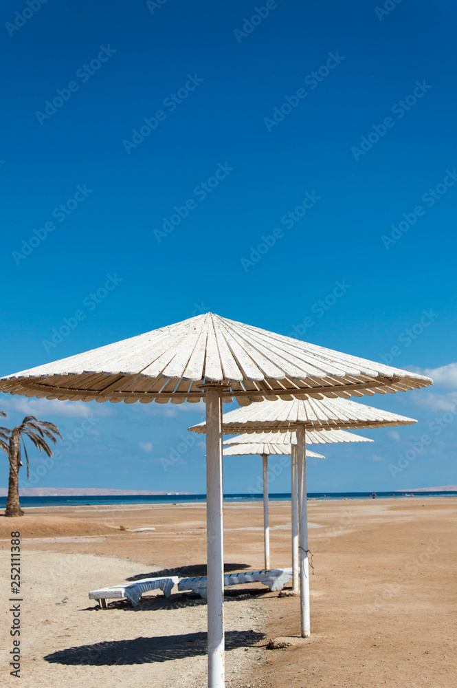 White parasols and sun loungers on the sandy beach by the sea.