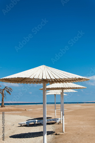 White parasols and sun loungers on the sandy beach by the sea.