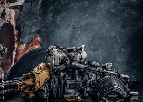 Military uniform and equipment. Body armor, gun, assault rifle, helmet, night vision goggles. Studio photo against a dark textured wall
