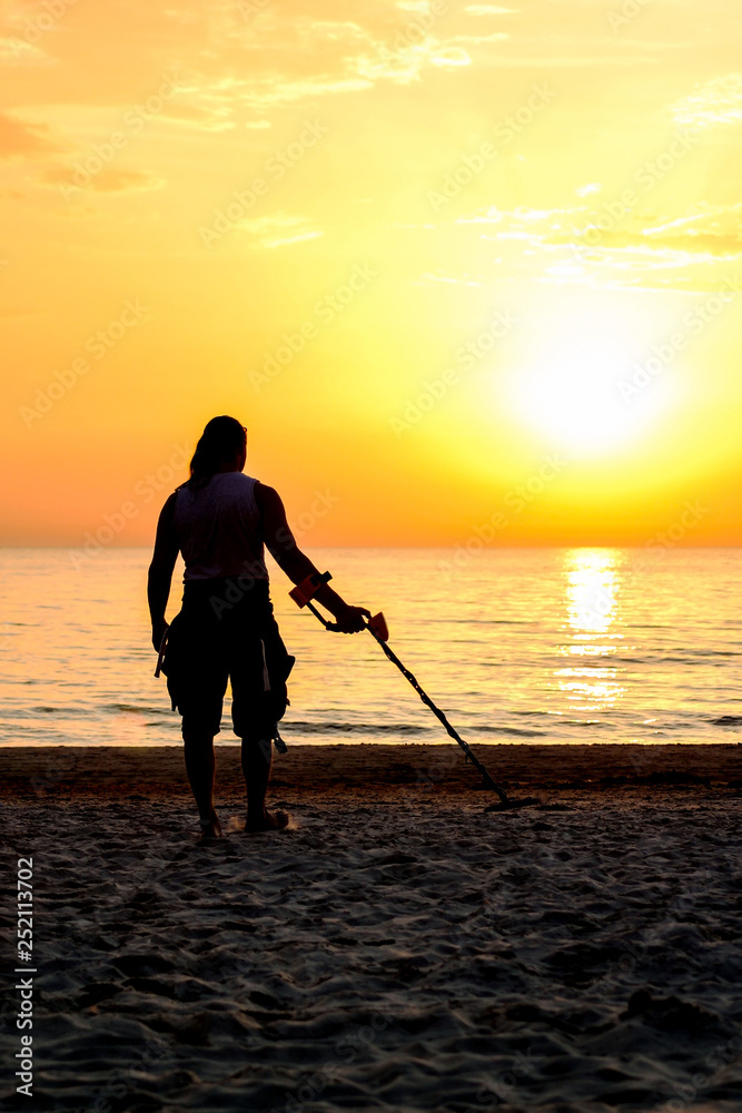 Man silhouette with metal detector on the beach