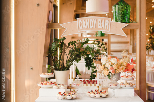 Candy bar with tasty desserts and appetizers at wedding reception. Decorated with flower compositions and candles. Sweet food, dessert, buffet, catering table, restaurant.