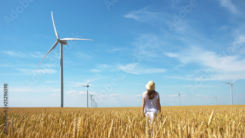 Beautiful girl on yellow field of wheat with windmills for electric power production