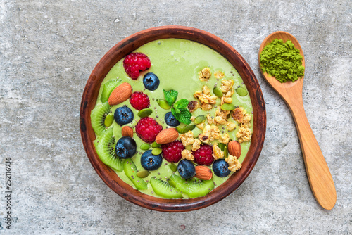 Smoothie bowl made of matcha green tea with fresh berries, nuts, seeds with a spoon for healthy vegan breakfast