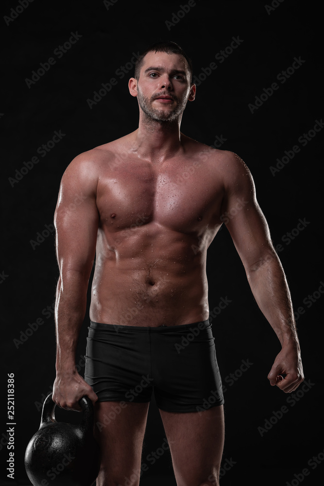 Handsome young man trains with dumbbells with water splashes on his face and chest in Studio shot