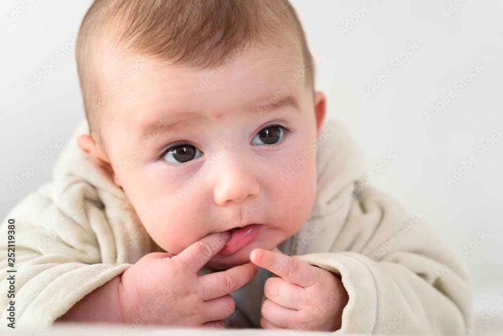 Portrait of an adorable smiling baby biting her own fingers putting her fist in her mouth.