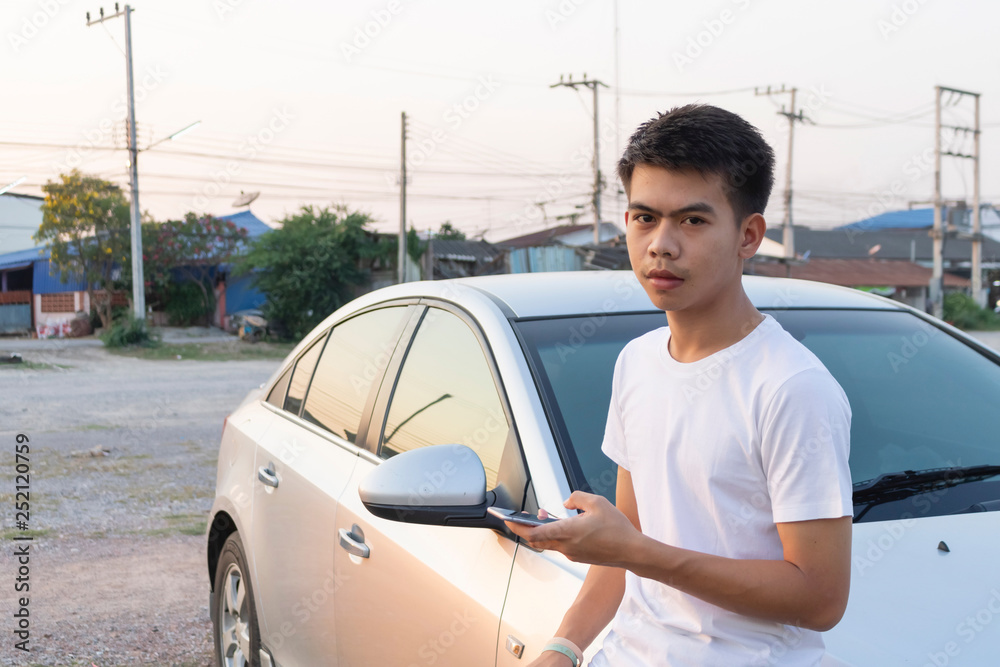 A boy iin white casual is chatting on his phone and leaning on the silver car hood. A boy iin white casual is chatting on his phone and leaning on the silver car hood.
