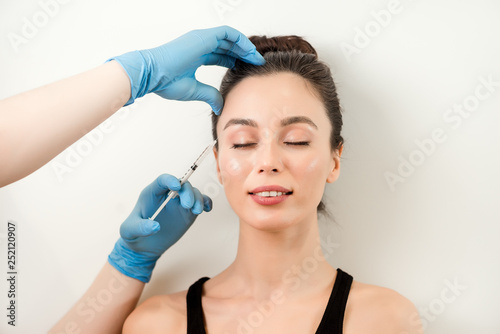 Medical doctor in blue gloves injecting woman in the face with a suringe