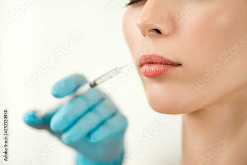 Close up of medical doctor in blue gloves injecting woman in the lips with a suringe
