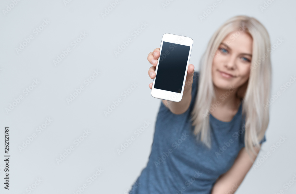 Teenage blond woman showing smartphone at camera 