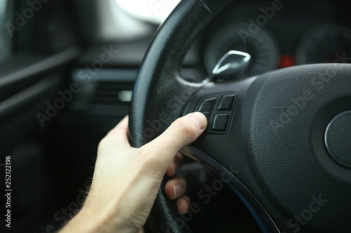 finger presses the button on the steering wheel of the car, speakerphone and cruise control. © velimir