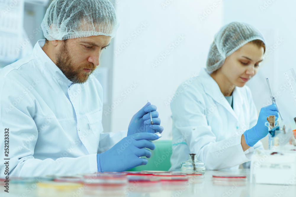 View of two friendly young scientists in lab coat making research in modern laboratory. Red haired siblings doing tests and checking results in private clinic. Medical workers working with reagents. View of two friendly young scientists in lab coat making research in modern laboratory. Red haired siblings doing tests and checking results in private clinic. Medical workers working with reagents.
