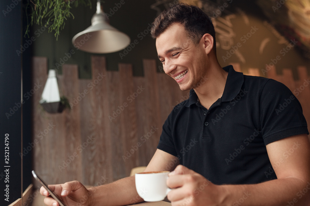 Cheerful guy with coffee browsing smartphone in cafe Cheerful guy with coffee browsing smartphone in cafe