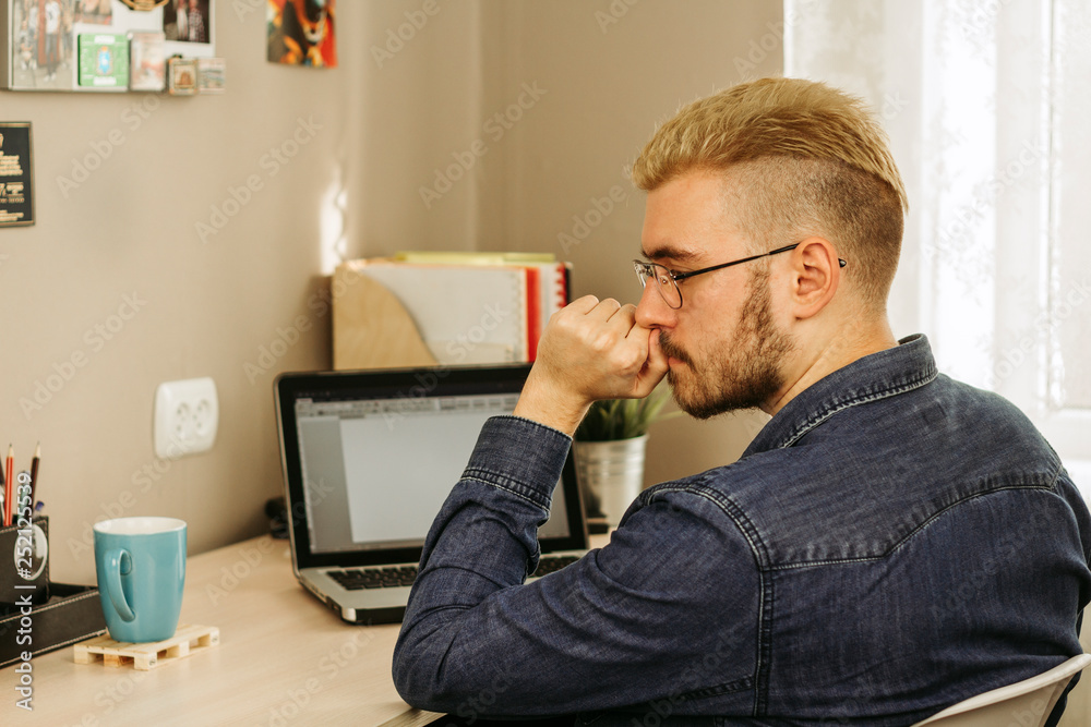 Side view of pensive man using laptop to work remotely at home via internet Side view of pensive man using laptop to work remotely at home via internet