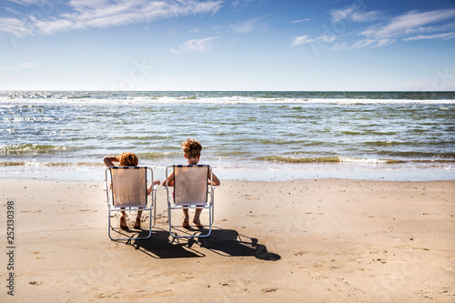 Netherlands, Zandvoort, boy and girl sitting on chairs on the beach