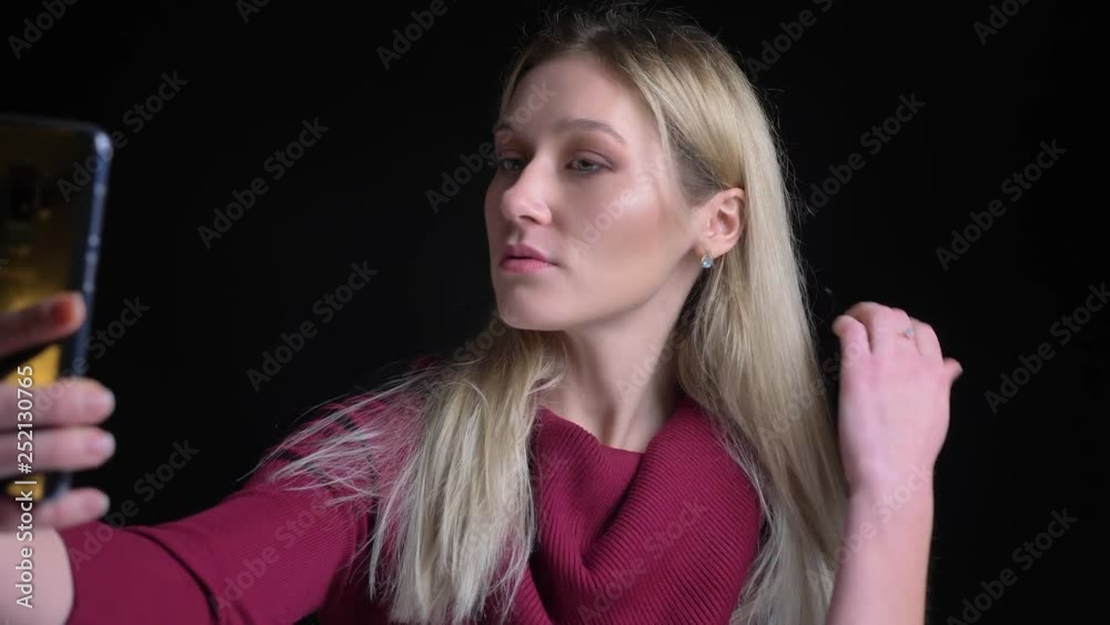 Closeup shoot of young pretty caucasian female taking selfies on the phone and posing in front of the camera Closeup shoot of young pretty caucasian female taking selfies on the phone and posing in front of the camera