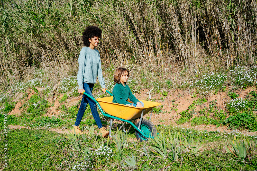 Father walking on a dirt track, pushing wheelbarrow, with his son sitting in it Father walking on a dirt track, pushing wheelbarrow, with his son sitting in it