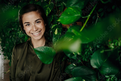 Portrait of smiling young woman at wall with climbing plants