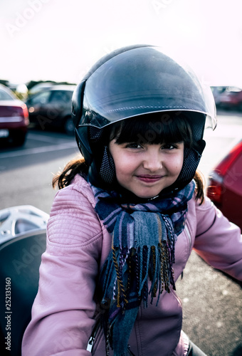 Portrait of smiling little girl on a motorcycle wearing helmet and pink leather jacket