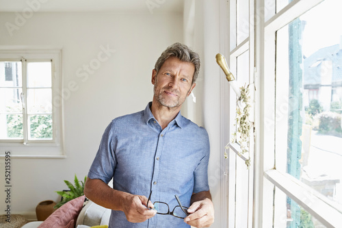 Mature man at home eaning at window, holding glasses photo