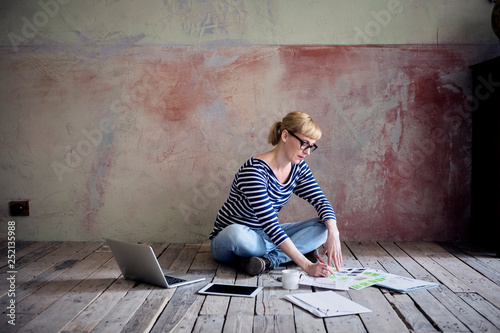Woman sitting on wooden floor in an unrenovated room of a loft working photo