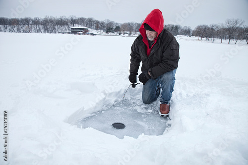 A middle aged man ice fishing on a lake in Minnesota during the winter
