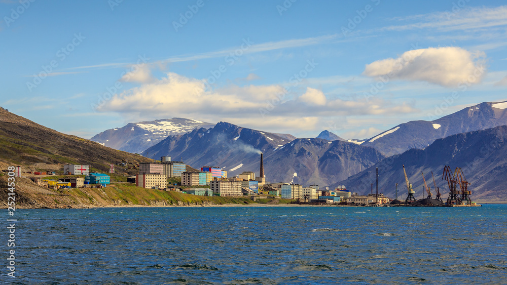 View from the sea on a small northern port town. Provideniya, Chukotka, Far East of Russia. Beautiful summer panorama of Providence Bay. In the distance, the picturesque mountains. Sunny weather.