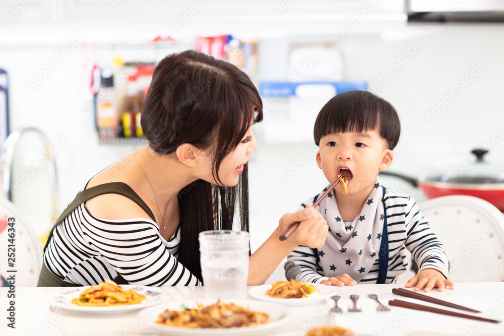 Mother and son in the kitchen, eating noodles together Mother and son in the kitchen, eating noodles together