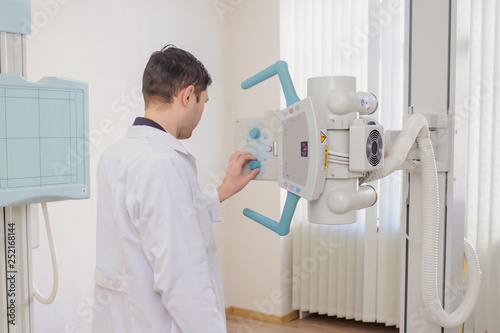  back view of a male radiologist adjusting the X-ray machine in examination rom photo