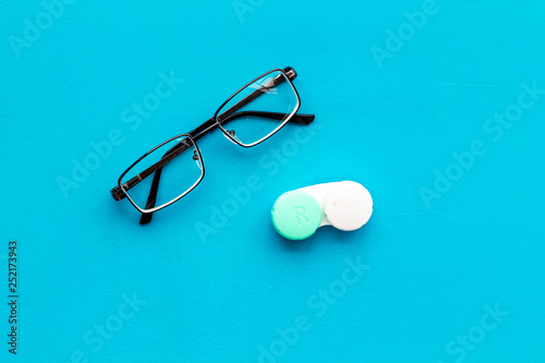 Eye problems. Glasses with transparent lenses and contact lenses on blue background top view copy space