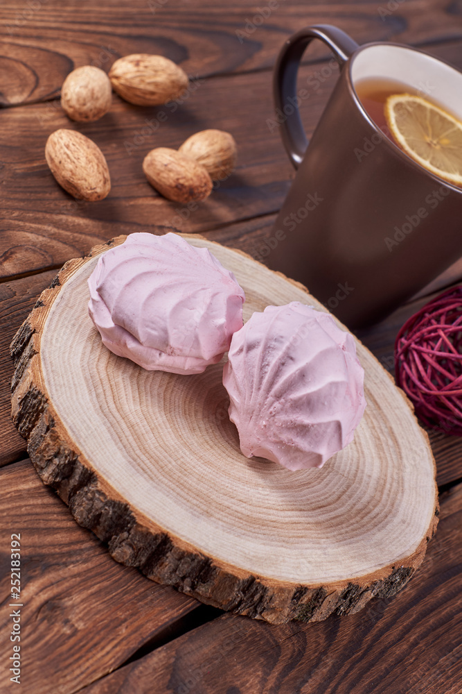 Two zephyrs with raspberries on a wooden stand next to brown cup with lemon tea, nuts and various decorative elements on the dark wooden background Two zephyrs with raspberries on a wooden stand next to brown cup with lemon tea, nuts and various decorative elements on the dark wooden background