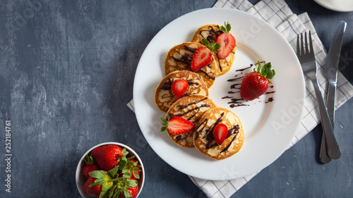 pancakes with strawberry and chocolate sauce on dark grey background. Copy space. Flat lay, top view