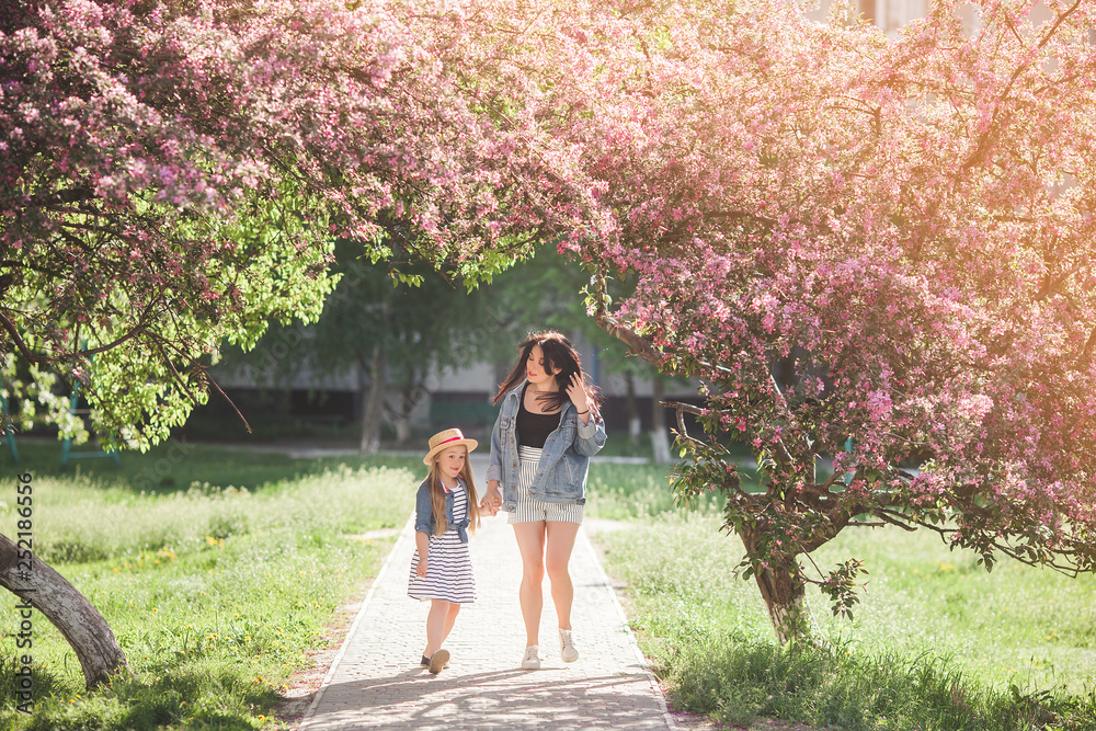 Naklejka premium Young attractive mother and her little daughter having fun together on spring background. Girls in flowers. Family outdoors. Summer mood.