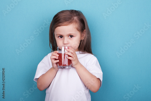 Cute little girl drinking juice from glass on blue background