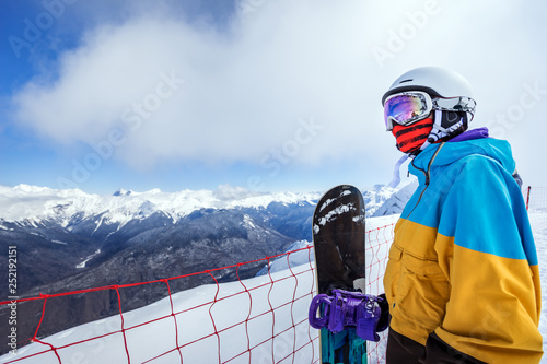 Portrait of woman snowboarder on background beautiful landscape of snowy high mountains of Caucasus at Krasnaya Polyana, standing with snowboard
