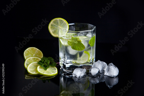 Summer cocktail mojito in glass, sliced lime and ice cubes on black background..
