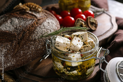Foto Glass jar with marinated cheese and tasty bread on wooden board, closeup