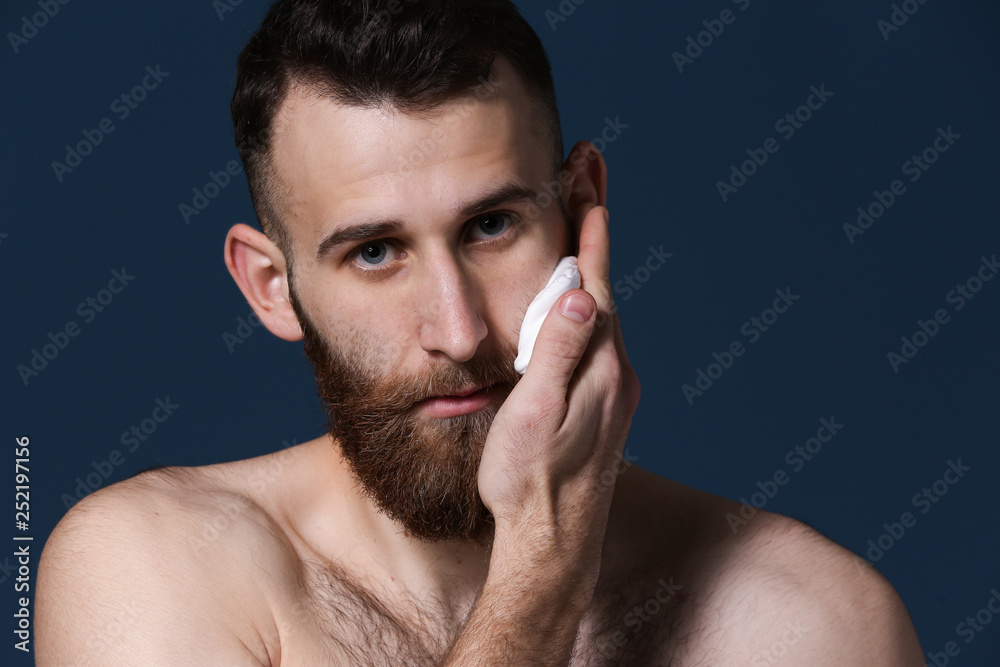 Obraz premium Bearded man applying shaving foam on dark background